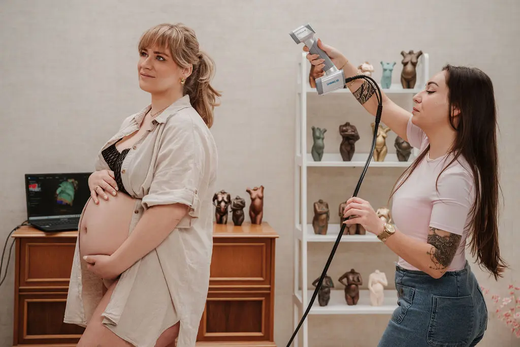 Zwangere vrouw wordt gescand door studio-eigenaar van buikbeeld tijdens het maken van een zwangerschapsbeeldje.